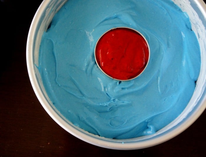 A close up of a round cake pan with blue cake batter and a small center pan with red cake batter
