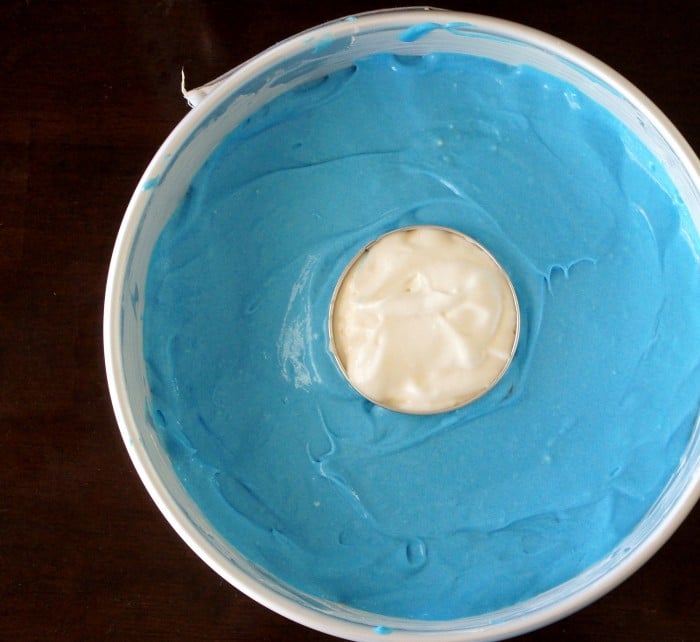 A close up of a round cake pan with blue cake batter and a small center pan with white cake batter