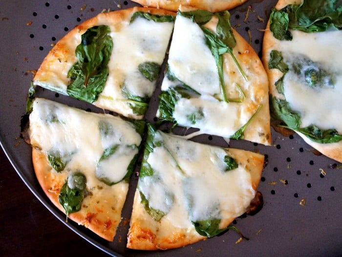 A close up of a pan with a sliced pita pizza topped with white sauce, cheese and spinach