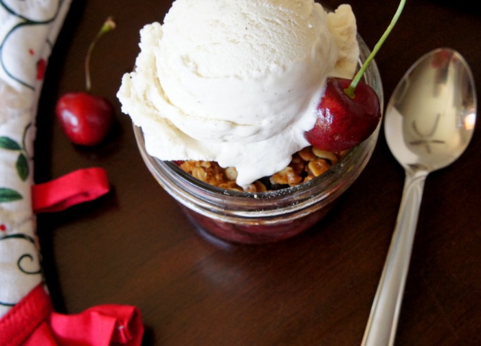 Cherry Crisp in a small glass mason jar topped with a scoop of ice cream and a fresh cherry on top