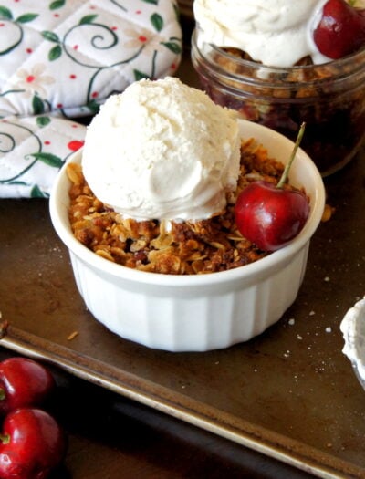 Cherry Crisp in a small dessert bowl topped with a scoop of ice cream with a fresh cherry on top