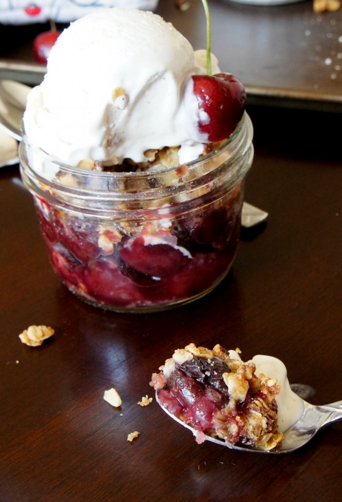 Cherry Crisp dessert in a small glass mason jar topped with a scoop of ice cream
