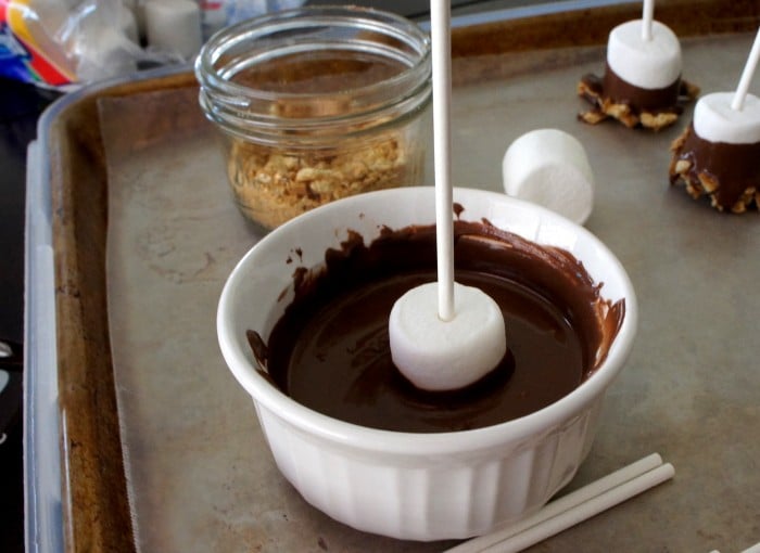 A marshmallow pop being dipped in a bowl of melted chocolate 