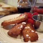 A display of french toast strips sprinkled with powdered sugar with a side of raspberries.