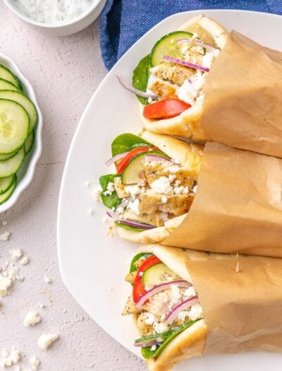 white plate with chicken souvlaki wrapped in pita bread with cucumbers.
