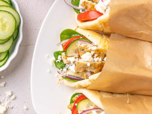 white plate with chicken souvlaki wrapped in pita bread with cucumbers.