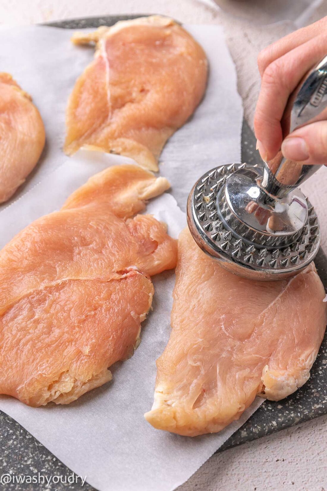 pounding chicken breast with metal tool.