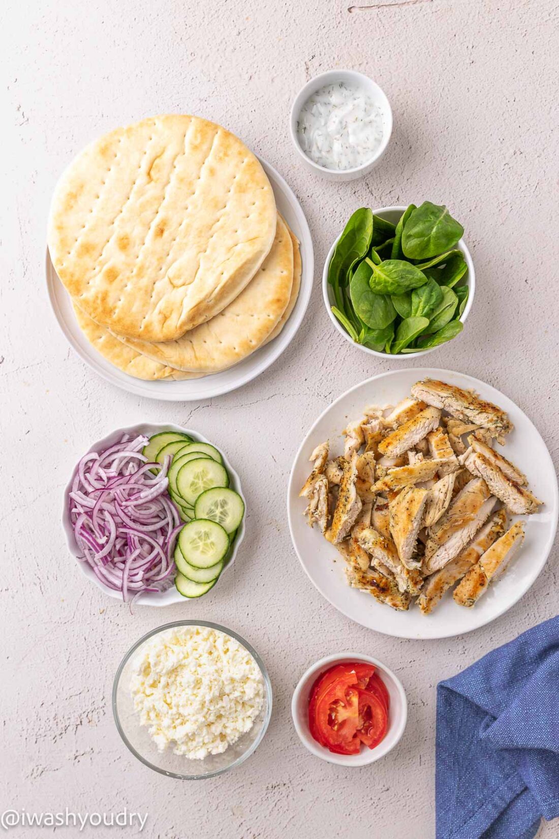 assembling grilled chicken souvlaki pitas with fresh ingredients on white surface.