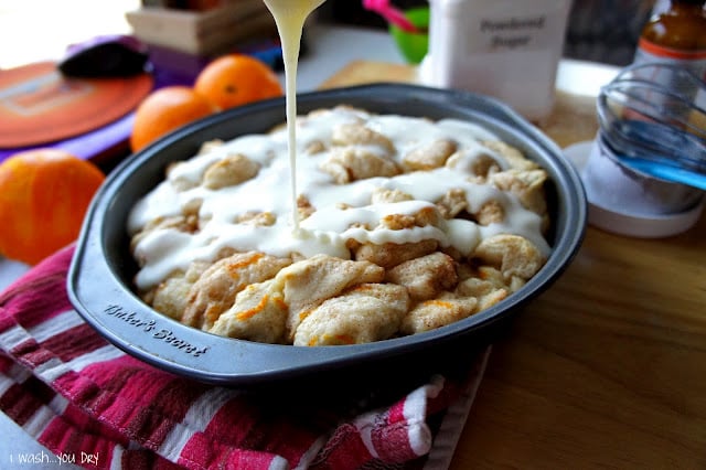 Icing being drizzled on top of a round pan of Orange Cinnamon Pull Apart