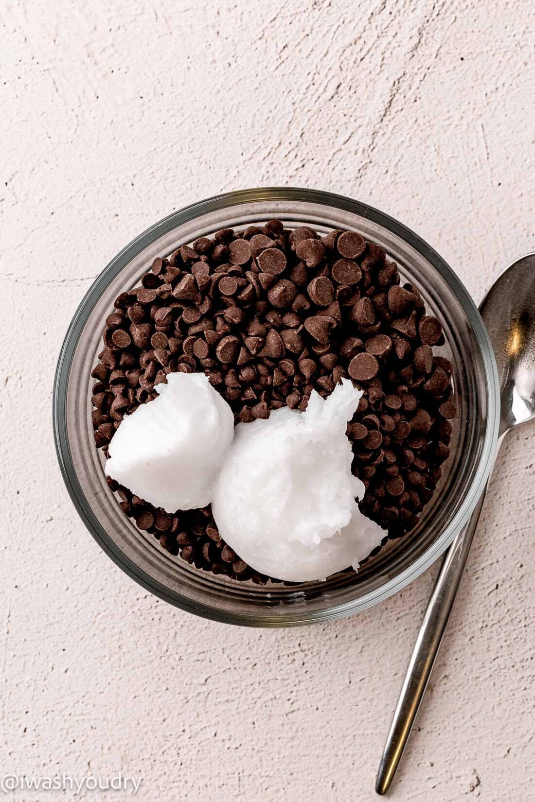 Glass bowl of chocolate chips and coconut oil with spoon. 