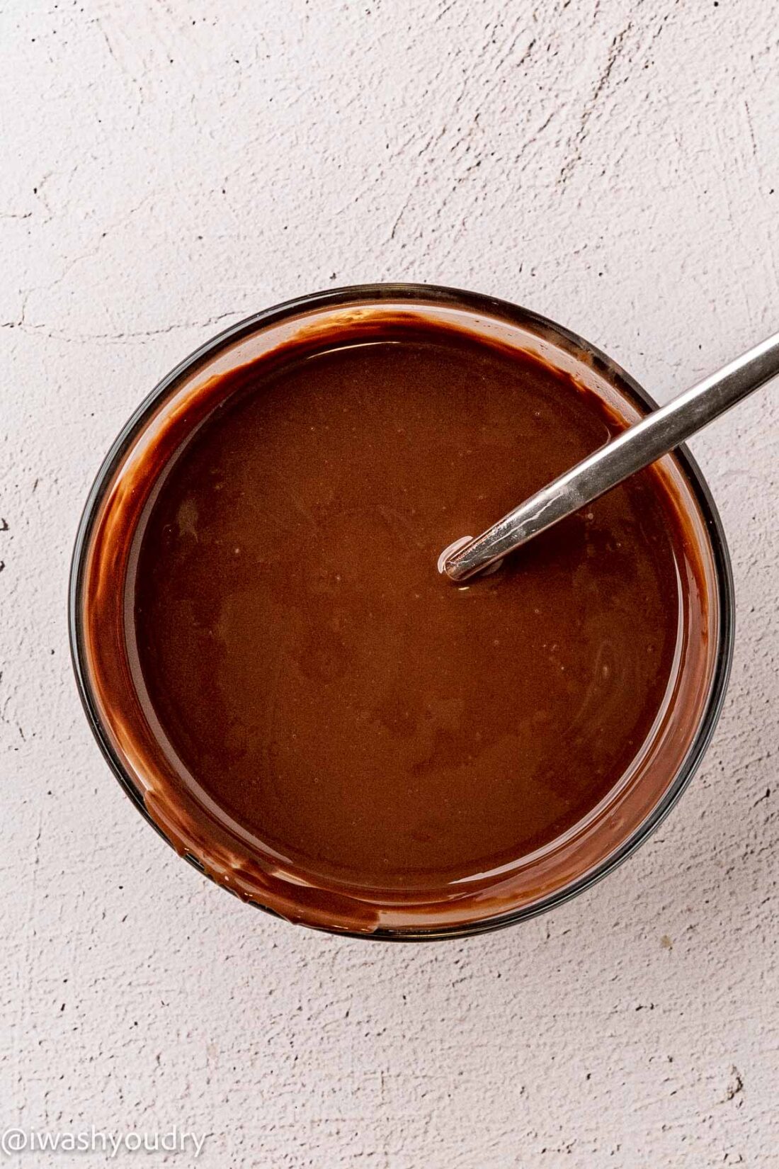 Glass bowl of melted chocolate and coconut oil with Spoon in bowl. 