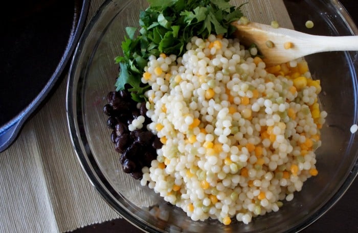 A spoon stirring herbs, couscous and beans in a glass bowl