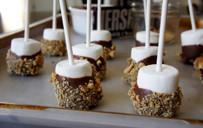 Marshmallow pops dipped in chocolate and graham cracker crumbs on a pan