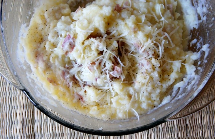 A close up of a bowl of mashed potatoes with shredded cheese on top