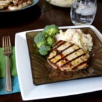 A plate with a grilled pork chop and sides of mashed potatoes and broccoli