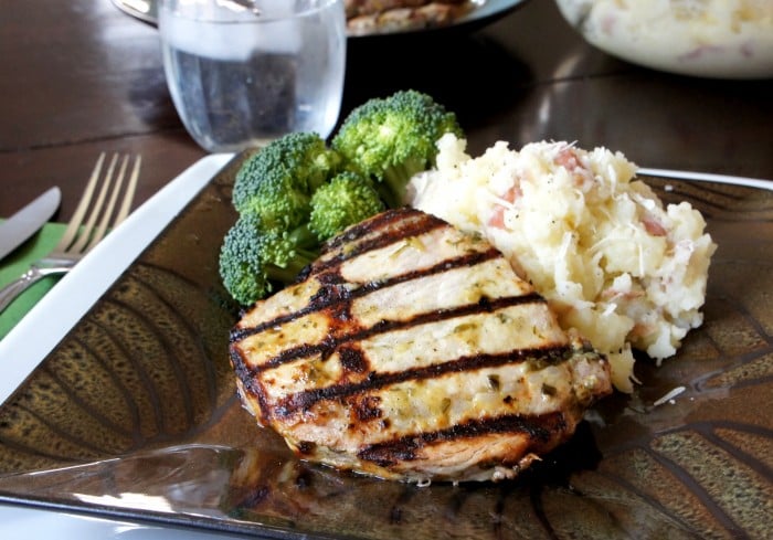 A close up of a grilled pork chop on a plate with a side of mashed potatoes and broccoli 