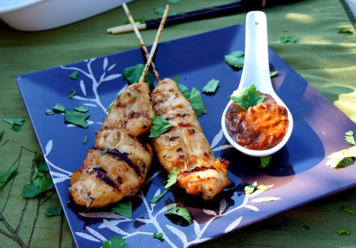 Two Thai Chicken tenders on skewers on a plate with a side of Spicy Peanut Dipping Sauce