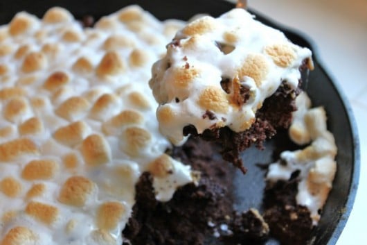 Brownies baked on a skillet topped with melted marshmallows with a slice being removed