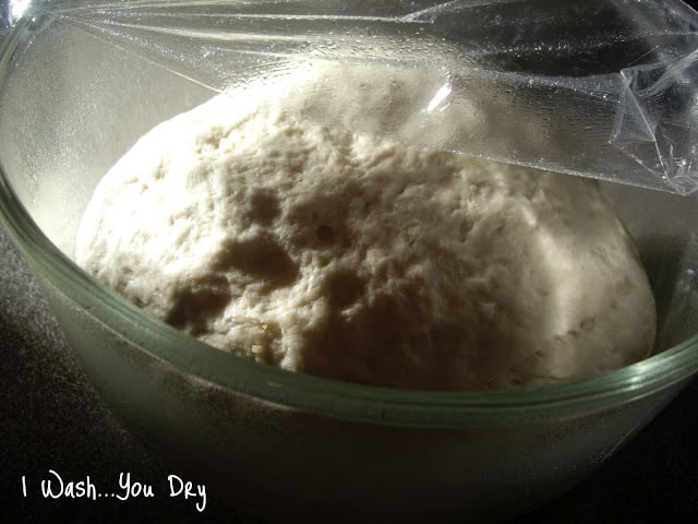 A ball of pizza dough in a dish covered with plastic wrap. 