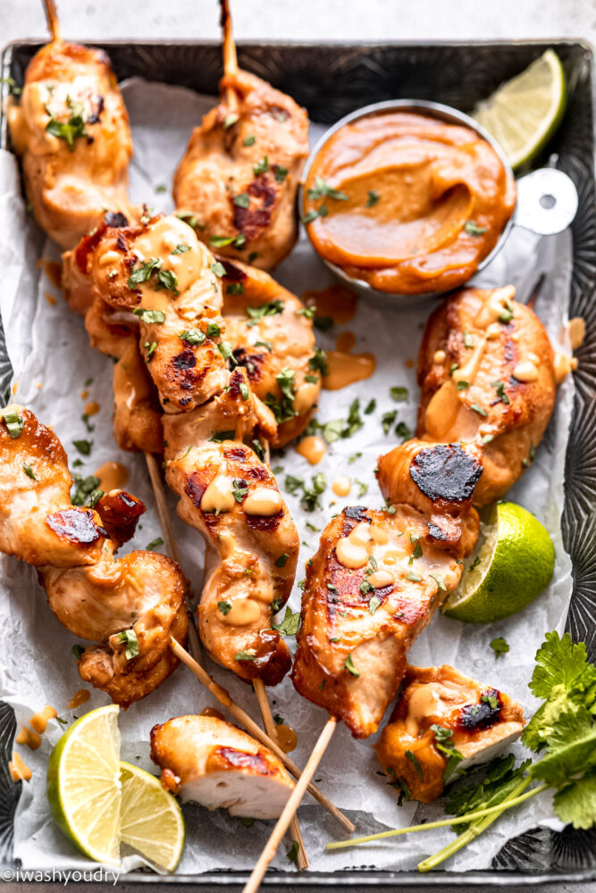 Cooked thai chicken satay on baking sheet with lime and peanut dipping sauce.