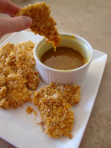 A hand dipping a Crunchy Baked Coconut Chicken