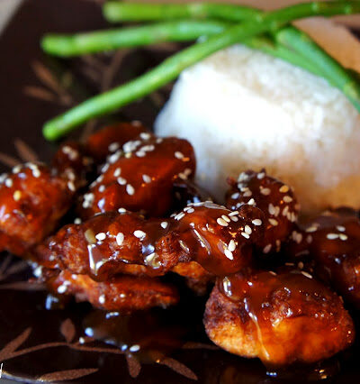 Sesame Chicken on plate next to a side of rice and asparagus sticks