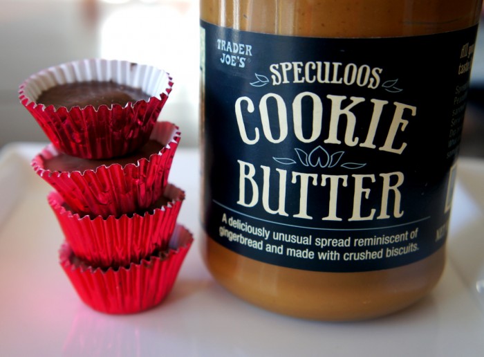 Four chocolates in red wrappers stacked on top of each other next to a jar of cookie butter
