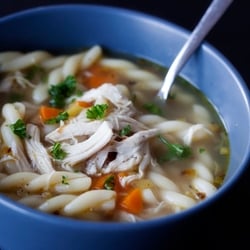 A close up of soup in a bowl with chicken, noodle and carrots 