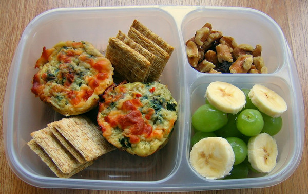 Bento lunch idea with a compartment for walnuts, a compartment for grapes and banana slices and crackers