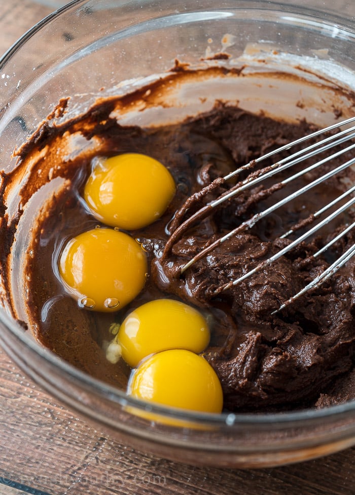 glass bowl with chocolate batter and eggs on top.
