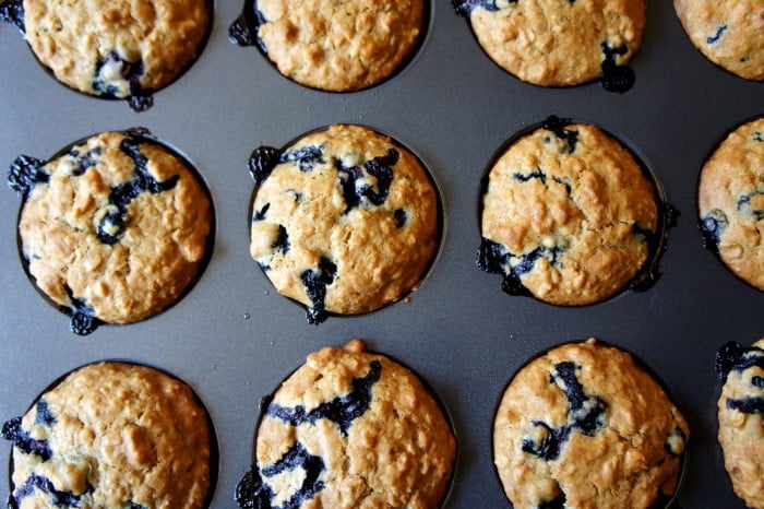 Close up of a pan of muffins, with blueberries drizzling from them