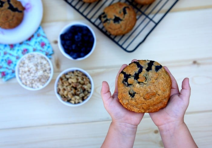 Two hands holding a Blueberry & Walnut Muffin above a table
