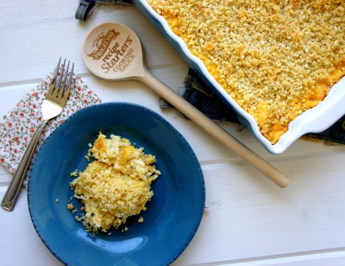 A scoop of casserole on a plate in front of a pan of Cheesy Zucchini and Potato Casserole