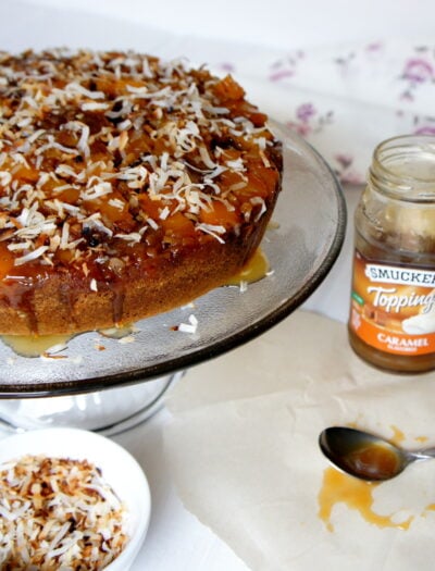A cake on a cake platter topped caramel and coconut flakes