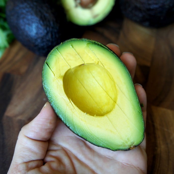 Half an avocado with slices made into it resting in a hand.