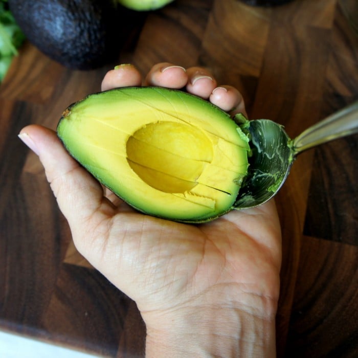 A hand holding half an avocado with a spoon removing the avocado from the skin