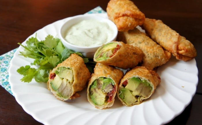 A plate with egg roll halves stuffed with avocado and a little bowl of dip
