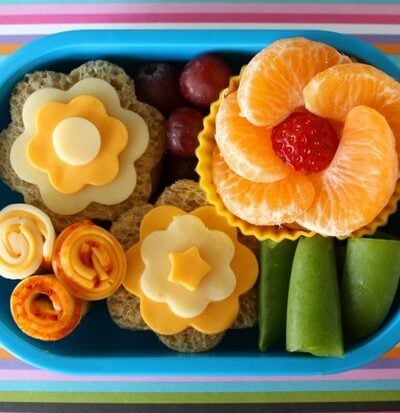 A bento lunch; sandwiches and fruit laid out to look like flowers