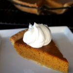 A slice of pumpkin pie on a plate with whipped cream on top