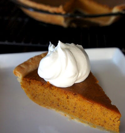 A slice of pumpkin pie on a plate with whipped cream on top