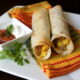 A close up of breakfast flautas displayed on a napkin, with sausage, egg and cheese in them