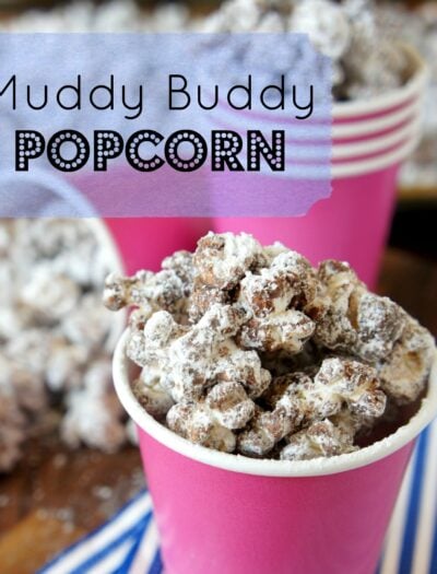 A pink cup full of Muddy Buddy Popcorn in front of other filled pink cups