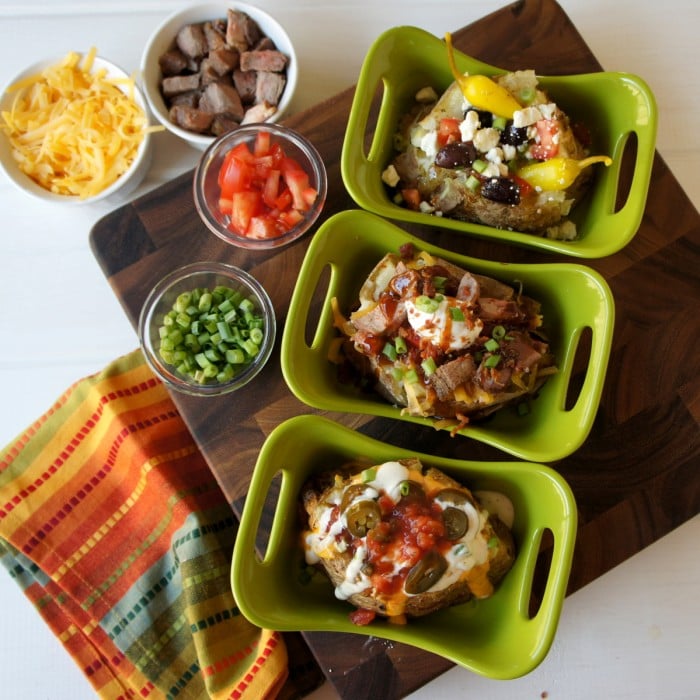 A look down on a three different baked potatoes with a variety of potatoes bar toppings