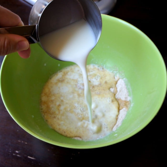 A measuring cup of milk being poured into a green mixing bowl