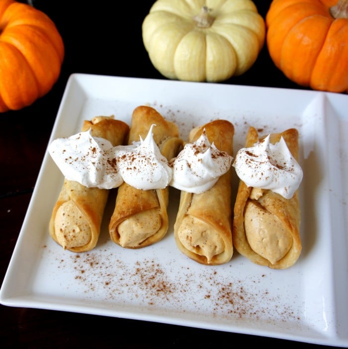 Four pumpkin pie cannolis on a plate topped with whipped cream and sprinkled with cinnamon