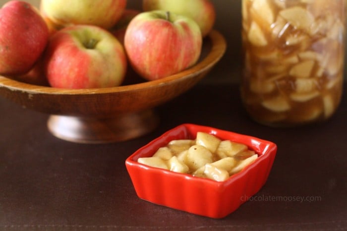 Homemade apple pie filling in a small dish in front of a bowl of apples and a jar of pie filling