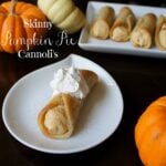 A plate displaying a Skinny Pumpkin Pie Cannoli in front of a larger platter with more cannolis