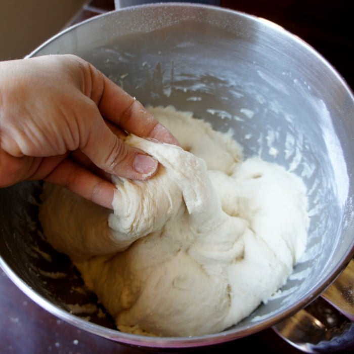 A mixing bowl with a hand pinching some dough in it. 