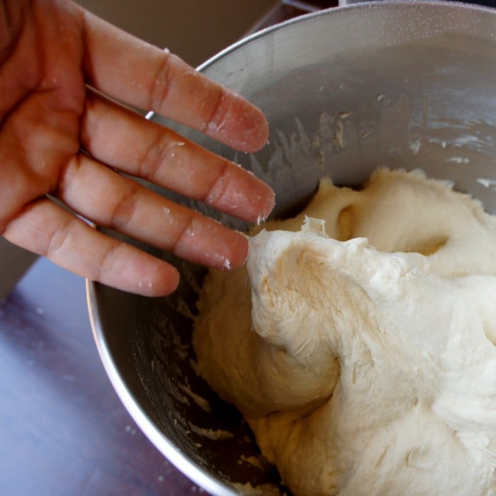 A close up of a mixing bowl with dough and a hand demonstrating the needed texture