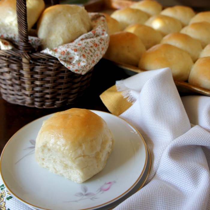 A plate with a baked roll on it in front of a basket and pan filled with baked rolls 